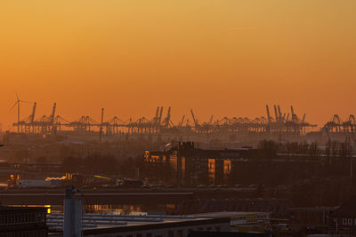 Cranes at commercial dock against sky during sunset