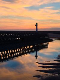 Silhouette wooden post by sea against sky during sunset