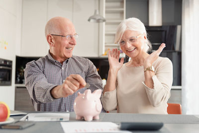 Senior couple inserting coin piggy bank over table