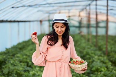 Smiling woman holding basket of strawberries at farm