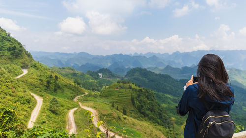 Rear view of man photographing on mountain against sky