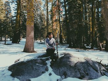 Man sitting on snow covered trees in forest