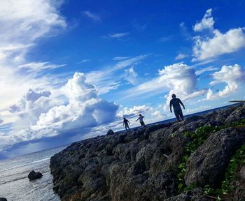 People standing on rock by sea against blue sky