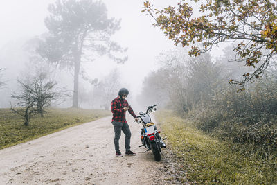 Man using smart phone while standing by motorcycle on dirt road