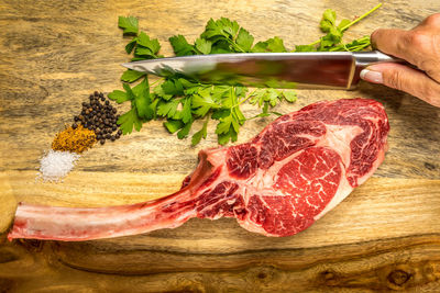 Cropped hand of woman holding kitchen knife by meat and ingredients on cutting board