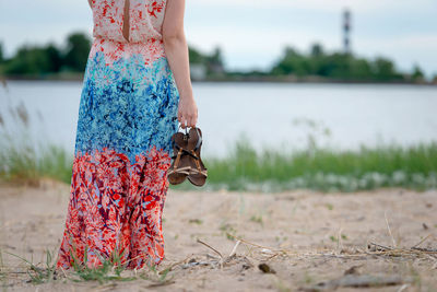 Midsection of woman holding sandals while standing on field