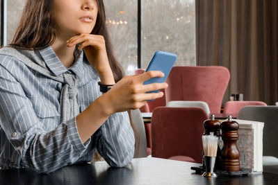 Young woman using phone while sitting in restaurant