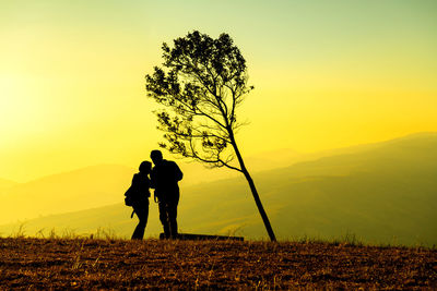Silhouette couple standing on land against sky during sunset