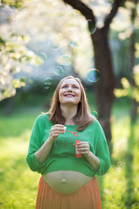Happy pregnant woman looking up at bubbles in park