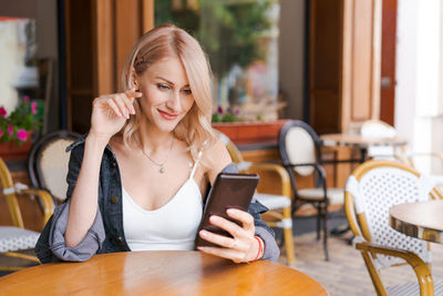 Young cute woman using phone sits in cafe at table with smartphone, answering