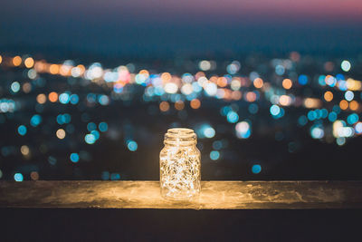 Close-up of illuminated string lights in glass jar on retaining wall at night