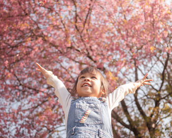 Low angle view of happy girl with arms raised against autumn trees in park