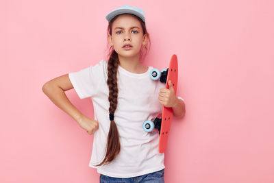 Portrait of young woman holding gift against pink background