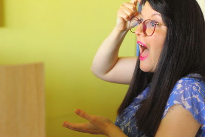 Portrait of woman wearing eyeglasses against wall