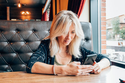 Portrait of smiling woman using phone while sitting on table