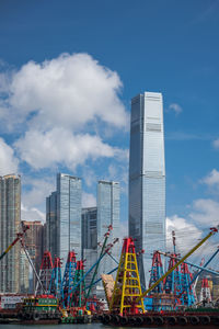 Ferris wheel by modern buildings in city against sky