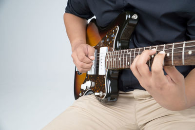 Midsection of musician playing guitar against white background