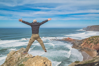 Man with arms raised on beach against sky