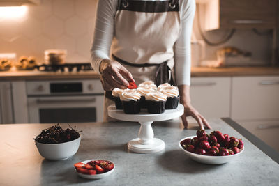 Woman decorate cupcakes with fruits and cream cheese closeup in kitchen. working at home. 