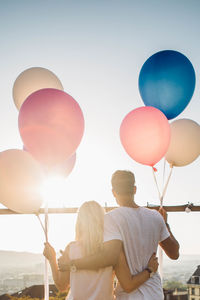 Rear view of couple standing with balloons against sky