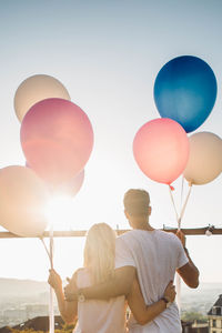 Rear view of men standing on balloons against sky