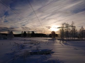 Snow covered field against sky during sunset