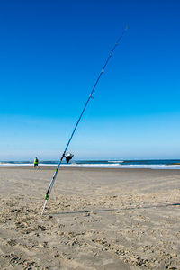 Fishing rod on beach against blue sky