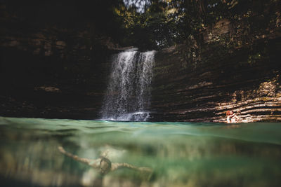 Man swimming in river against waterfall