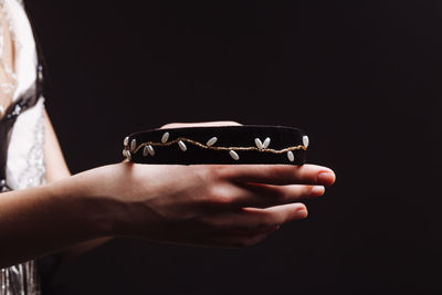 Close-up of hand holding bracelet against black background