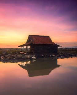 Built structure by lake against sky during sunset