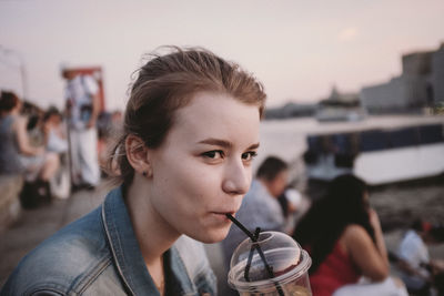 Close-up of young woman drinking from disposable cup at sunset