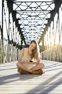 Woman listening music while sitting on bridge in city