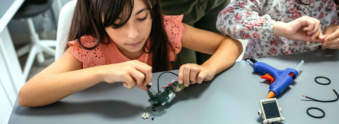 Student screwing electrical circuit next to schoolchild in robotics class