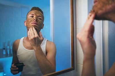 Man applying mask on face while looking in mirror at home