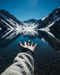 Cropped hand gesturing towards lake and snowcapped mountain against clear sky