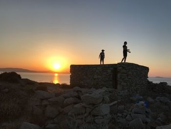 Silhouette people on rock against sky during sunset