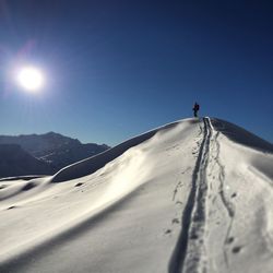 Low angle view of a man walking on snow against blue sky
