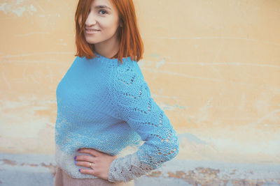 Portrait of smiling young woman standing against wall