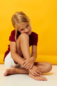 Young woman sitting on hardwood floor against yellow background