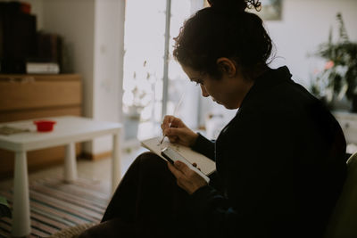 Side view of woman using mobile phone and sketching at home