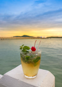 Close-up of beer in glass against sea during sunset