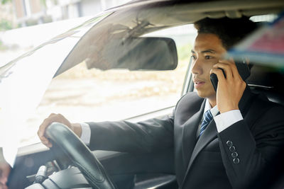 Businessman talking on phone seen through windshield while driving car