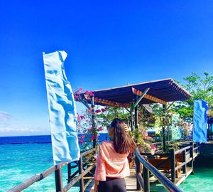 Rear view of woman walking on pier in sea against blue sky