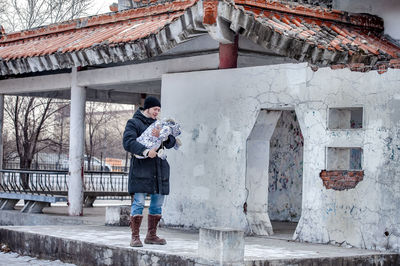 Young father standing against the wall of a building with baby on his hands