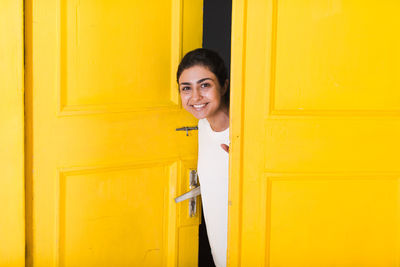 Portrait of smiling young woman against yellow door