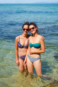 Portrait of smiling female friends wearing bikinis standing in sea