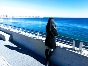 Man on railing by sea against sky