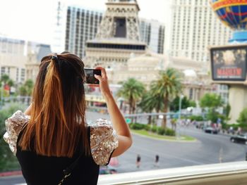 Rear view of woman photographing with mobile phone in city