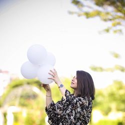 Portrait of young woman holding balloons against sky