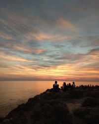 People looking at sea against sky during sunset